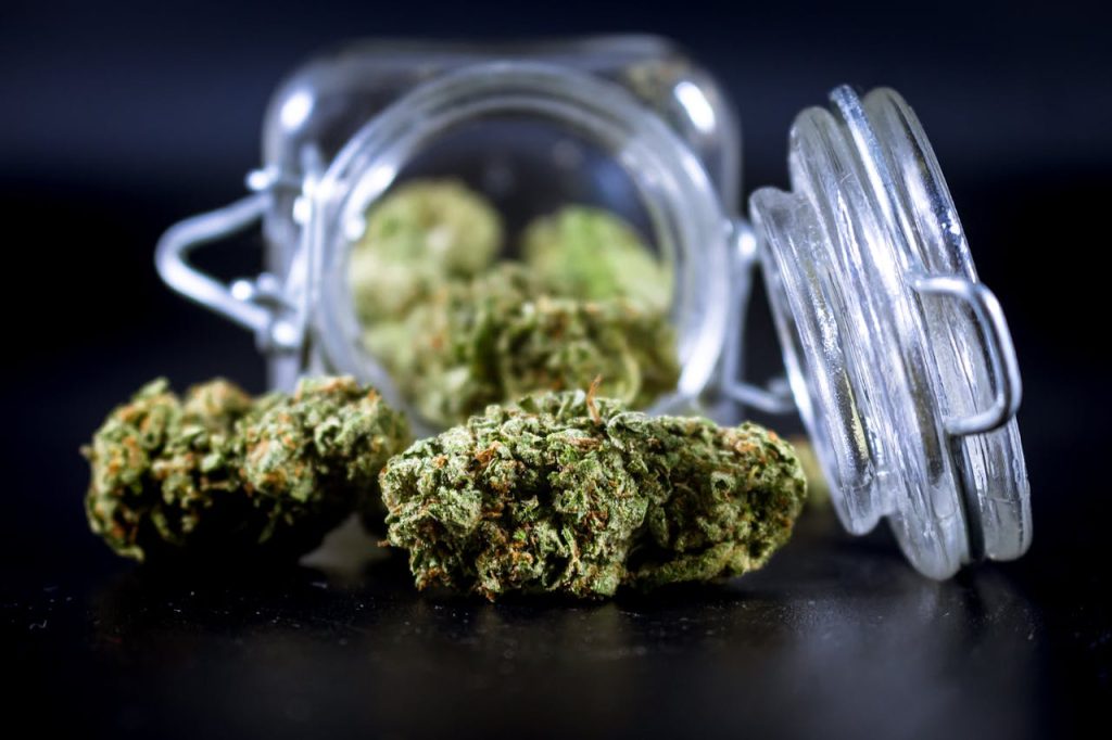 High-quality image of cannabis buds partially spilling from an open glass jar.